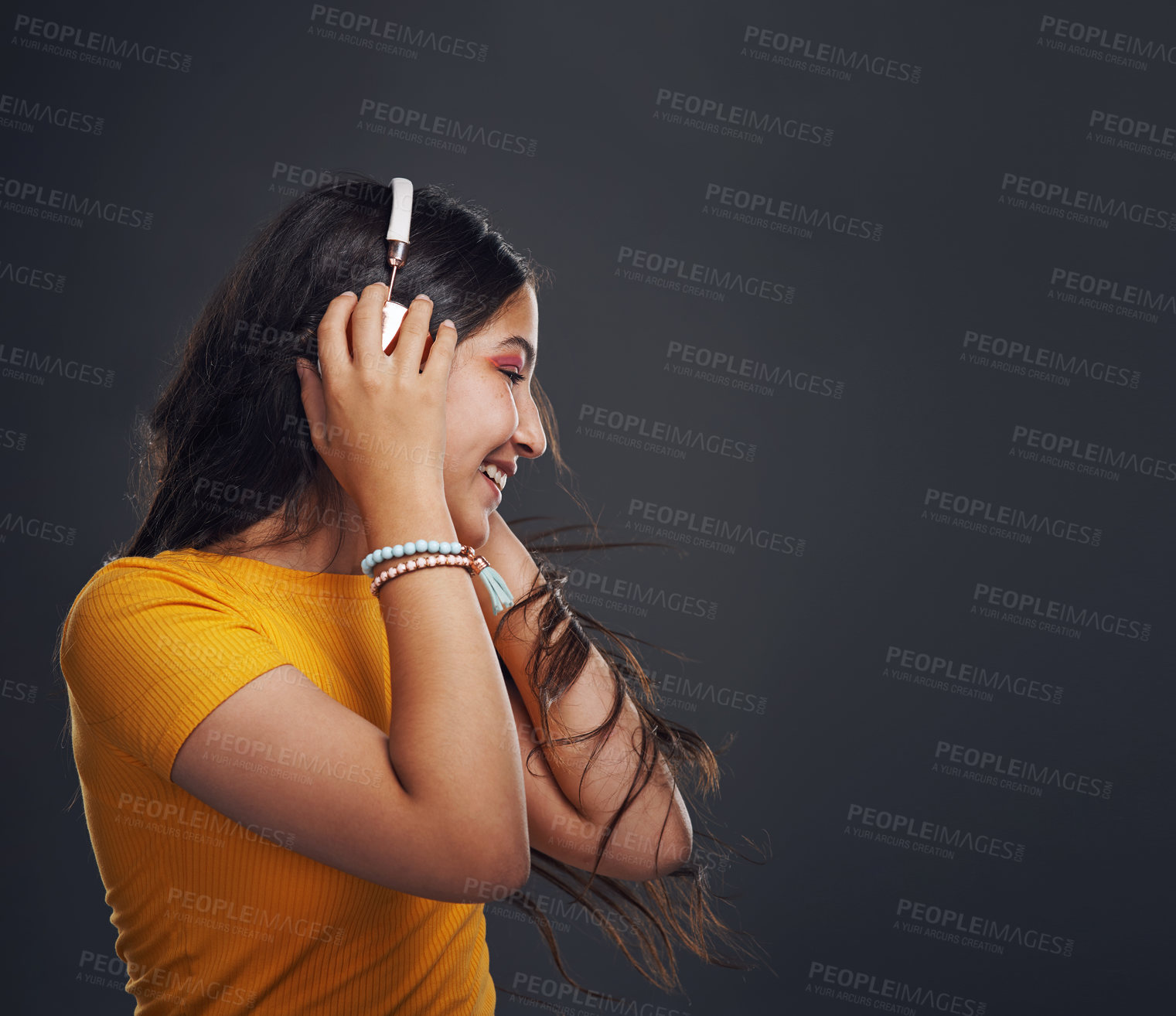 Buy stock photo Cropped shot of an attractive teenage girl standing against a dark background alone and listening to music through headphones