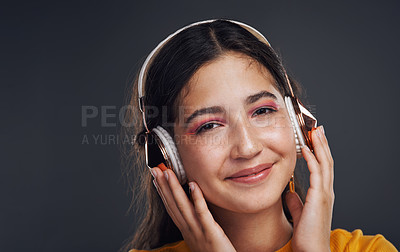Buy stock photo Cropped portrait of an attractive teenage girl standing against a dark background alone and listening to music through headphones