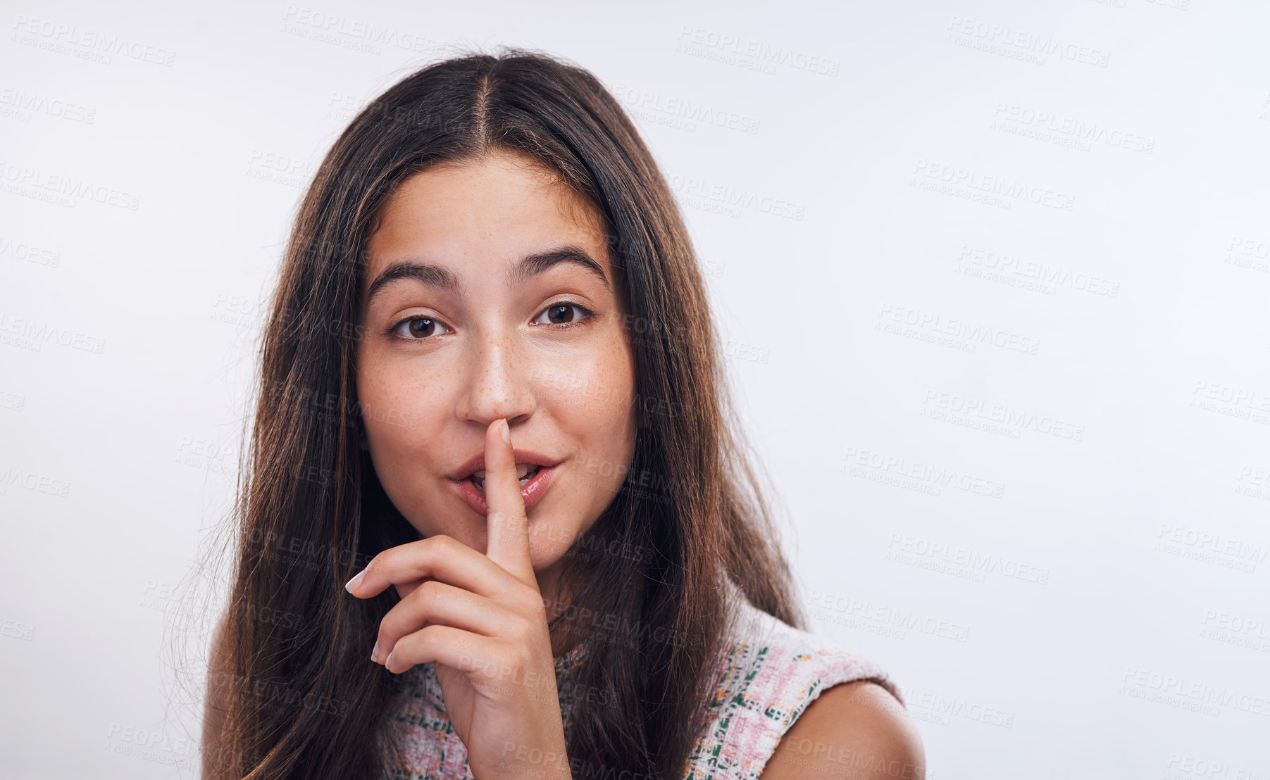 Buy stock photo Cropped portrait of an attractive teenage girl standing with her finger on her lips against a white studio background
