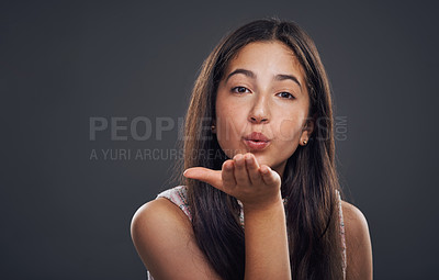 Buy stock photo Cropped portrait of an attractive teenage girl standing alone and blowing kisses against a dark studio background
