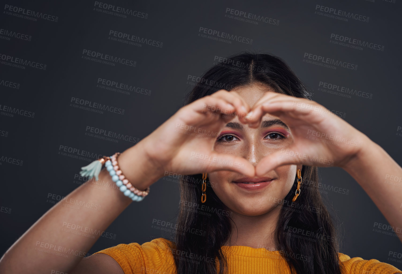 Buy stock photo Cropped portrait of an attractive teenage girl making a heart-shaped hand gesture against a dark studio background