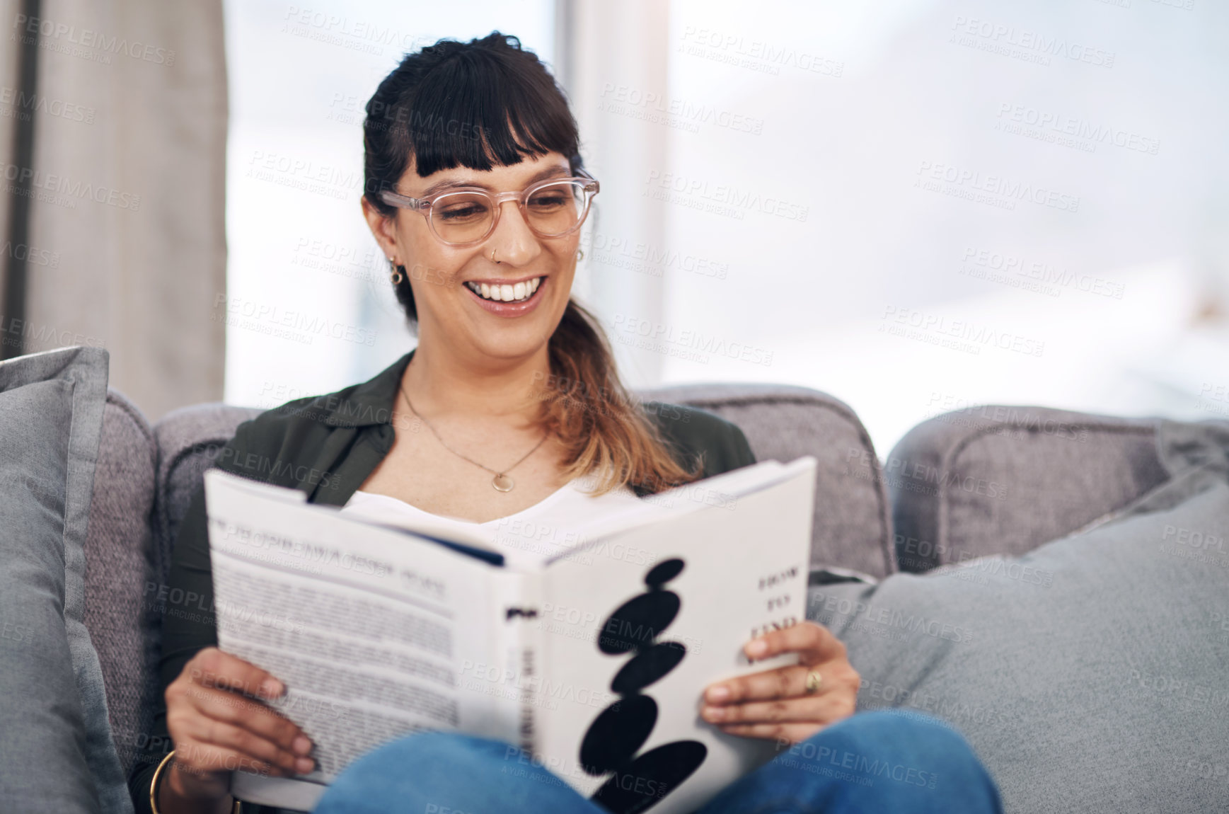 Buy stock photo Cropped shot of an attractive young woman sitting alone in her living room and reading a book