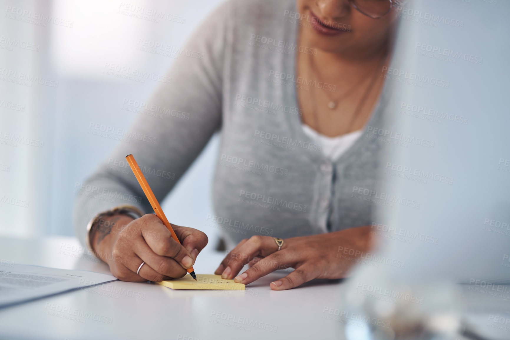 Buy stock photo Cropped shot of an unrecognizable businesswoman sitting alone in her office and writing on a post-it