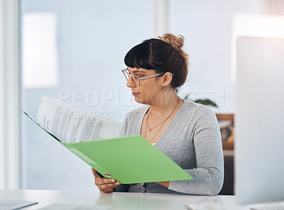 Buy stock photo Cropped shot of an attractive young businesswoman sitting alone in her office and reading through paperwork