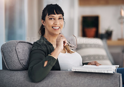 Buy stock photo Cropped portrait of an attractive young woman sitting alone in her living room and reading a book
