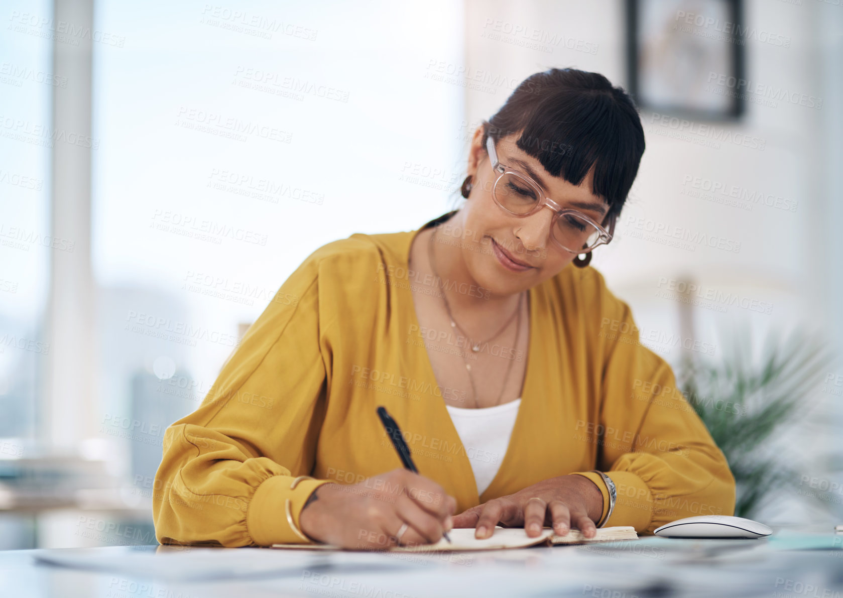 Buy stock photo Cropped shot of an attractive young businesswoman sitting alone in her office and writing in a notebook
