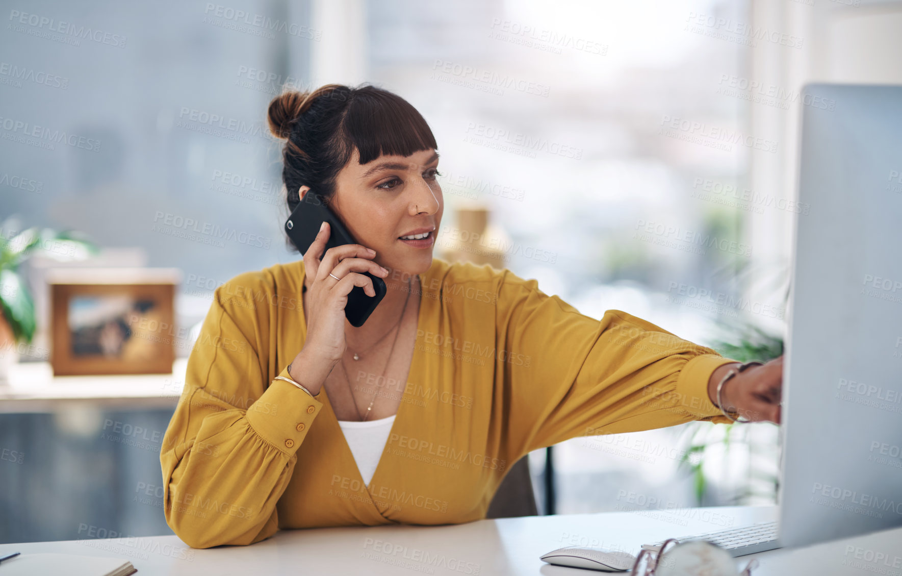 Buy stock photo Cropped shot of attractive young businesswoman sitting alone in her office talking on her cellphone while using her computer