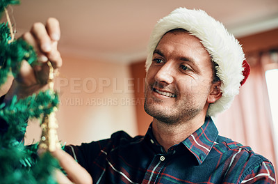 Buy stock photo Shot of a happy young man decorating his Christmas tree at home