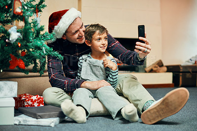 Buy stock photo Shot of an adorable little boy taking selfies with his father while unwrapping Christmas presents at home