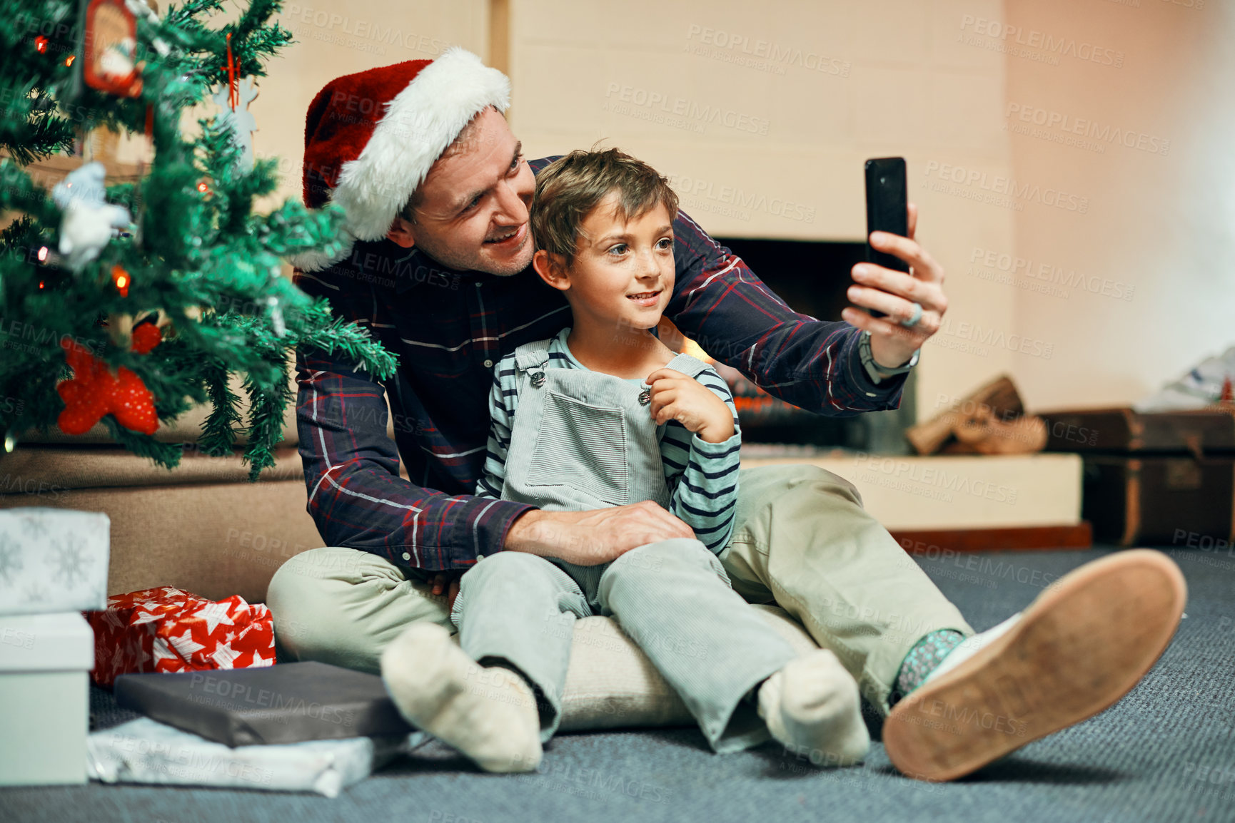 Buy stock photo Shot of an adorable little boy taking selfies with his father while unwrapping Christmas presents at home