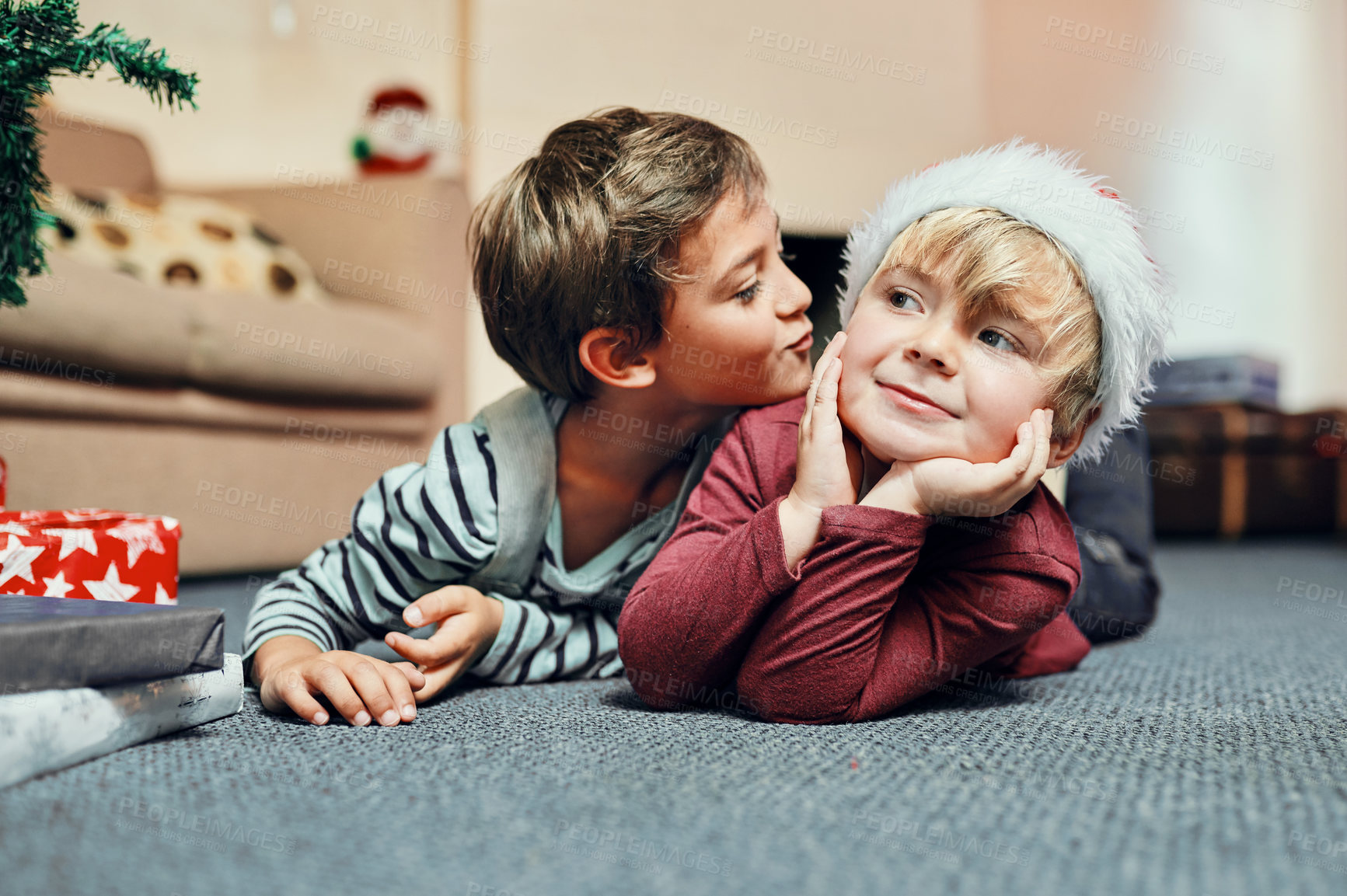 Buy stock photo Shot of an adorable little boy giving his brother a kiss while waiting to open their Christmas presents