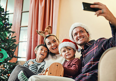 Buy stock photo Shot of a happy young family of four taking selfies during Christmas at home