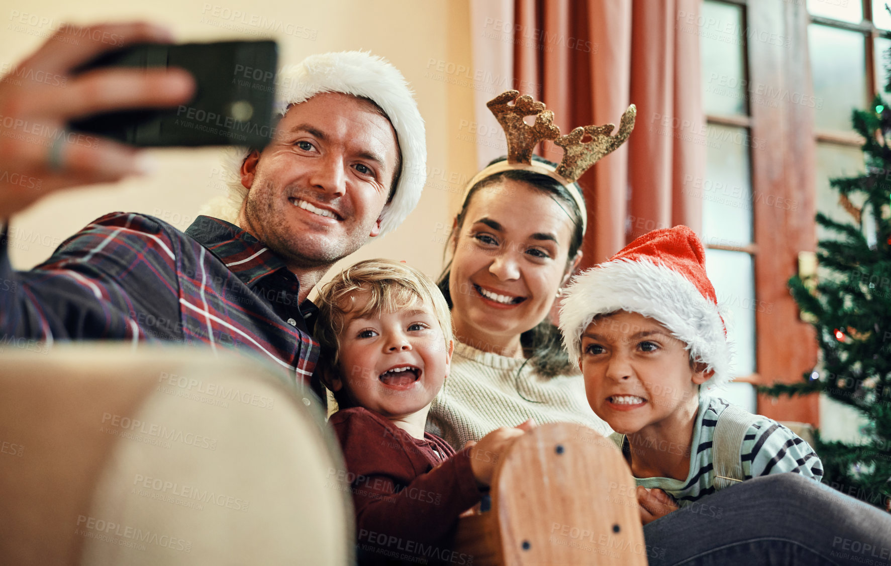 Buy stock photo Shot of a happy young family of four taking selfies during Christmas at home