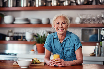 Buy stock photo Cropped portrait of an attractive senior woman enjoying a glass of orange juice while preparing breakfast in the kitchen