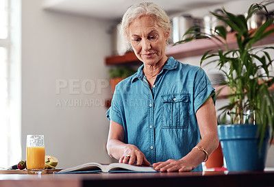 Buy stock photo Cropped shot of an attractive senior woman reading from a recipe book while preparing breakfast in the kitchen