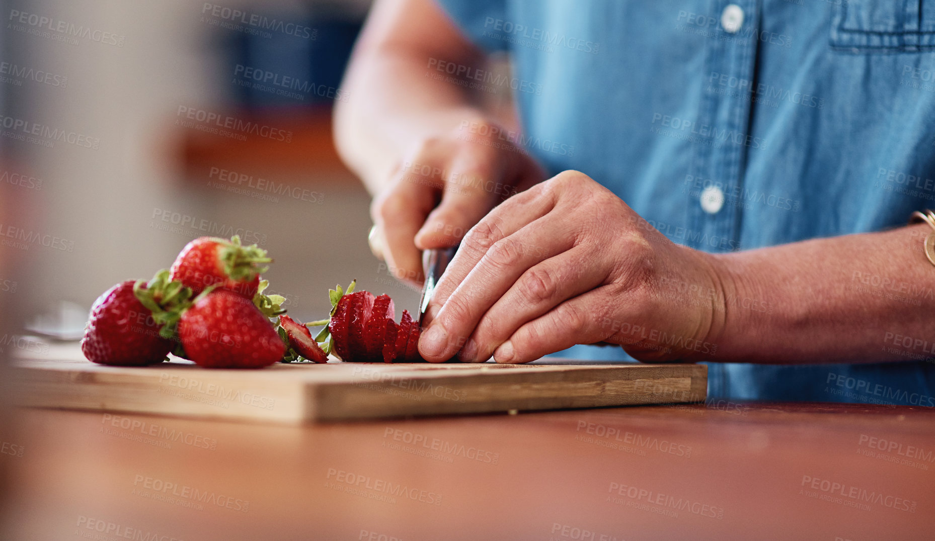 Buy stock photo Cropped shot of an unrecognizable senior woman cutting up strawberries while preparing breakfast in her kitchen at home