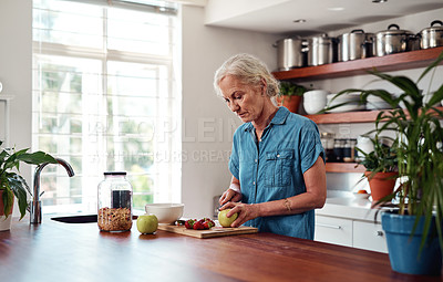 Buy stock photo Cropped shot of an attractive senior woman chopping up apples and other fruit while preparing breakfast in the kitchen