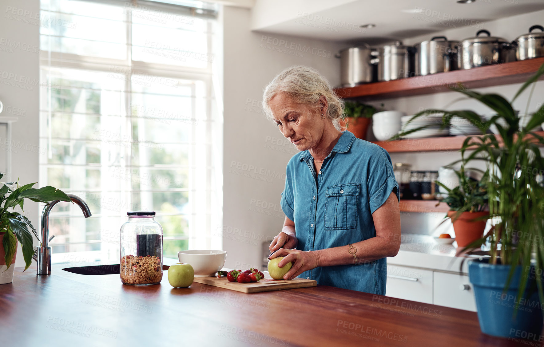 Buy stock photo Cropped shot of an attractive senior woman chopping up apples and other fruit while preparing breakfast in the kitchen