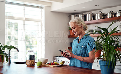 Buy stock photo Cropped shot of an attractive senior woman sending text messages while preparing breakfast in the kitchen at home