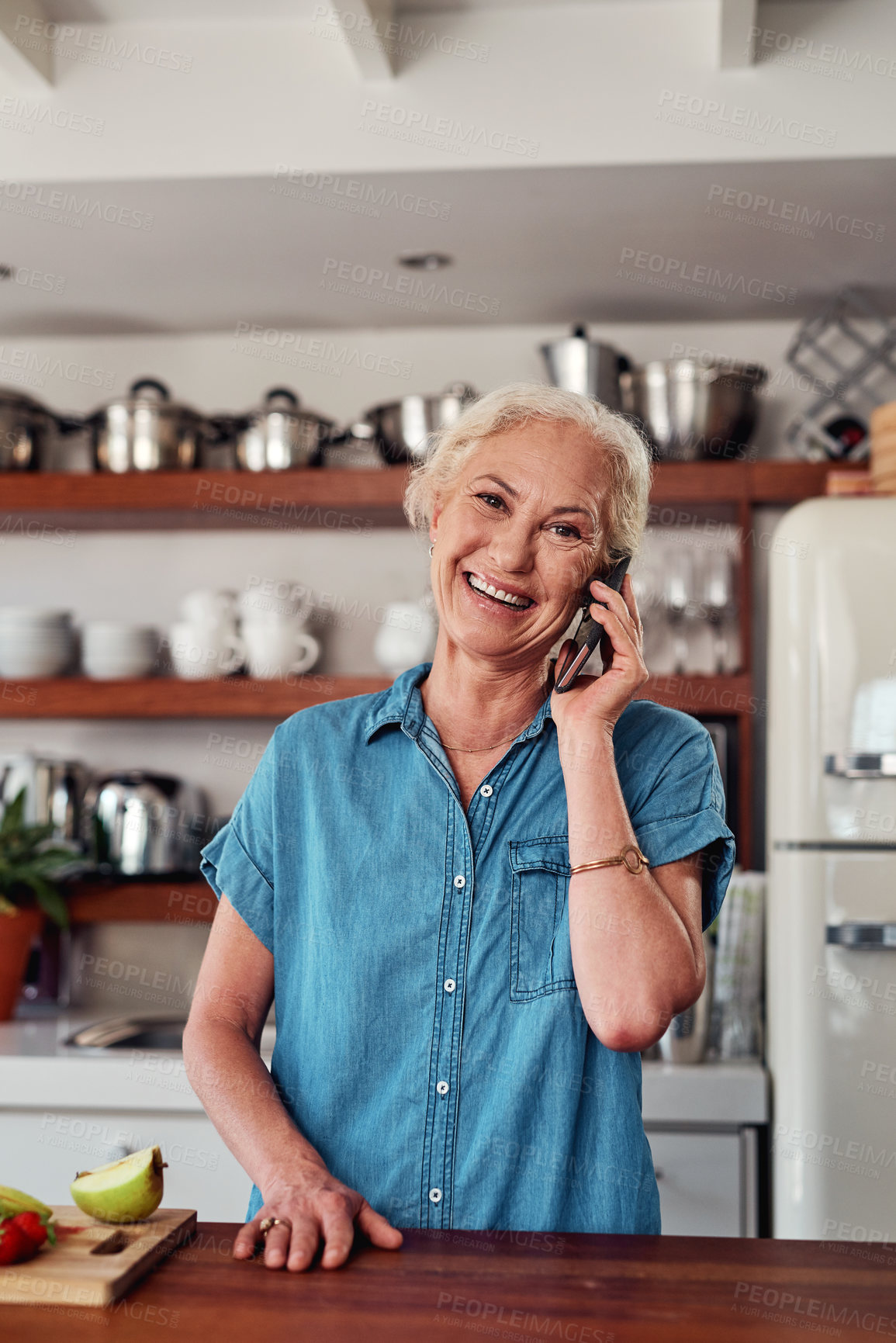 Buy stock photo Cropped portrait of an attractive senior woman making a phonecall while preparing breakfast in the kitchen at home