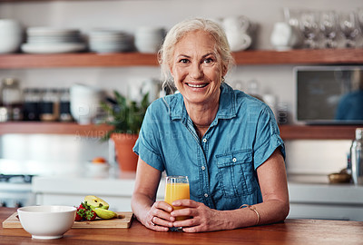 Buy stock photo Cropped portrait of an attractive senior woman enjoying a glass of orange juice while preparing breakfast in the kitchen at home