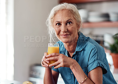Buy stock photo Cropped portrait of an attractive senior woman enjoying a glass of orange juice while standing in her kitchen at home