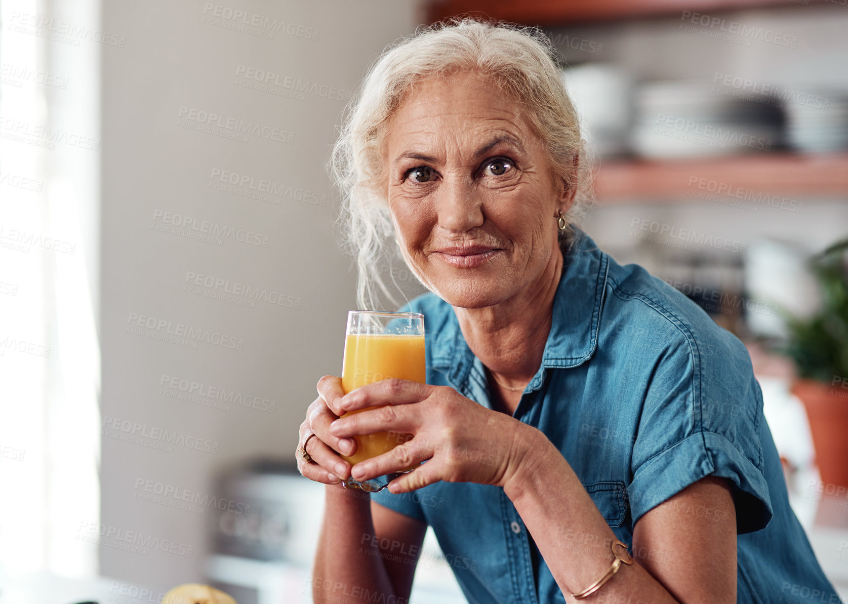 Buy stock photo Cropped portrait of an attractive senior woman enjoying a glass of orange juice while standing in her kitchen at home