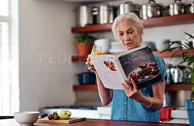 Buy stock photo Cropped shot of an attractive senior woman reading from a recipe book while preparing breakfast in the kitchen at home