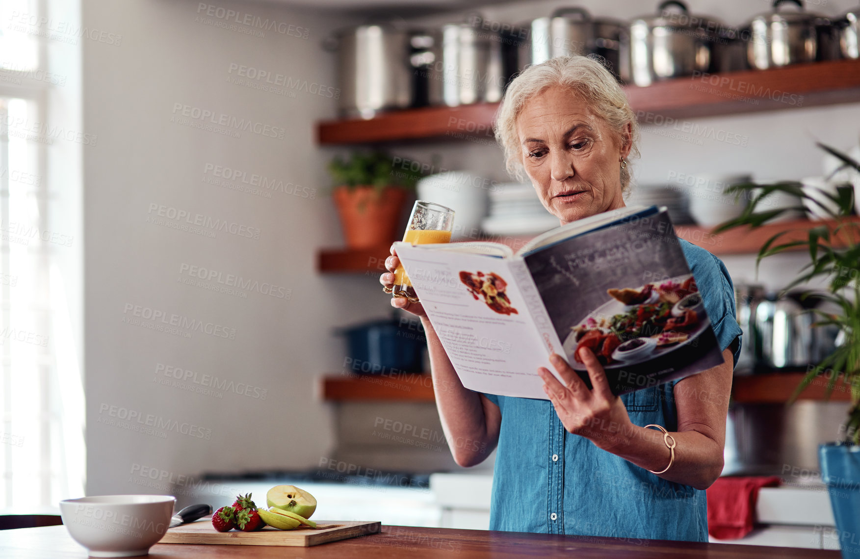 Buy stock photo Cropped shot of an attractive senior woman reading from a recipe book while preparing breakfast in the kitchen at home