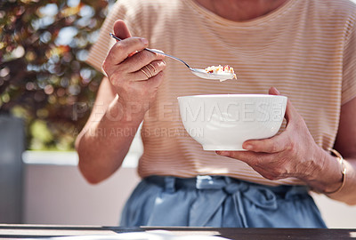 Buy stock photo Cropped shot of an unrecognizable senior woman enjoying her breakfast while sitting outside on the balcony at home