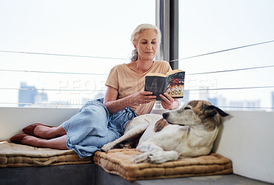 Buy stock photo Full length shot of an attractive senior woman reading a book while relaxing on the balcony with her dog