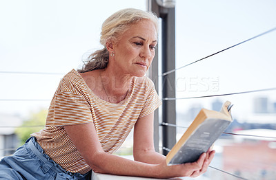 Buy stock photo Cropped shot of an attractive senior woman reading a book while relaxing on her balcony at home