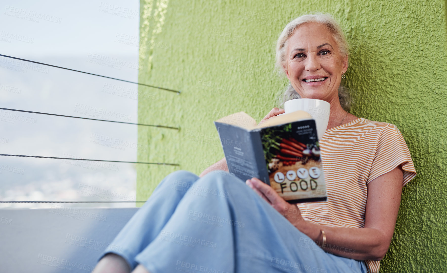 Buy stock photo Cropped shot of an attractive senior woman enjoying a cup of coffee and looking contemplative while reading a book outside on her balcony