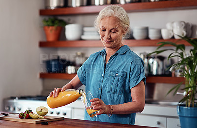 Buy stock photo Cropped shot of an attractive senior woman pouring herself a glass of orange juice while preparing breakfast in the kitchen