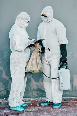 Buy stock photo Shot of two healthcare workers wearing hazmat suits working together during an outbreak in the city