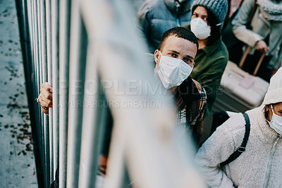 Buy stock photo Shot of a group of young people wearing masks while stuck behind a gate in a foreign city