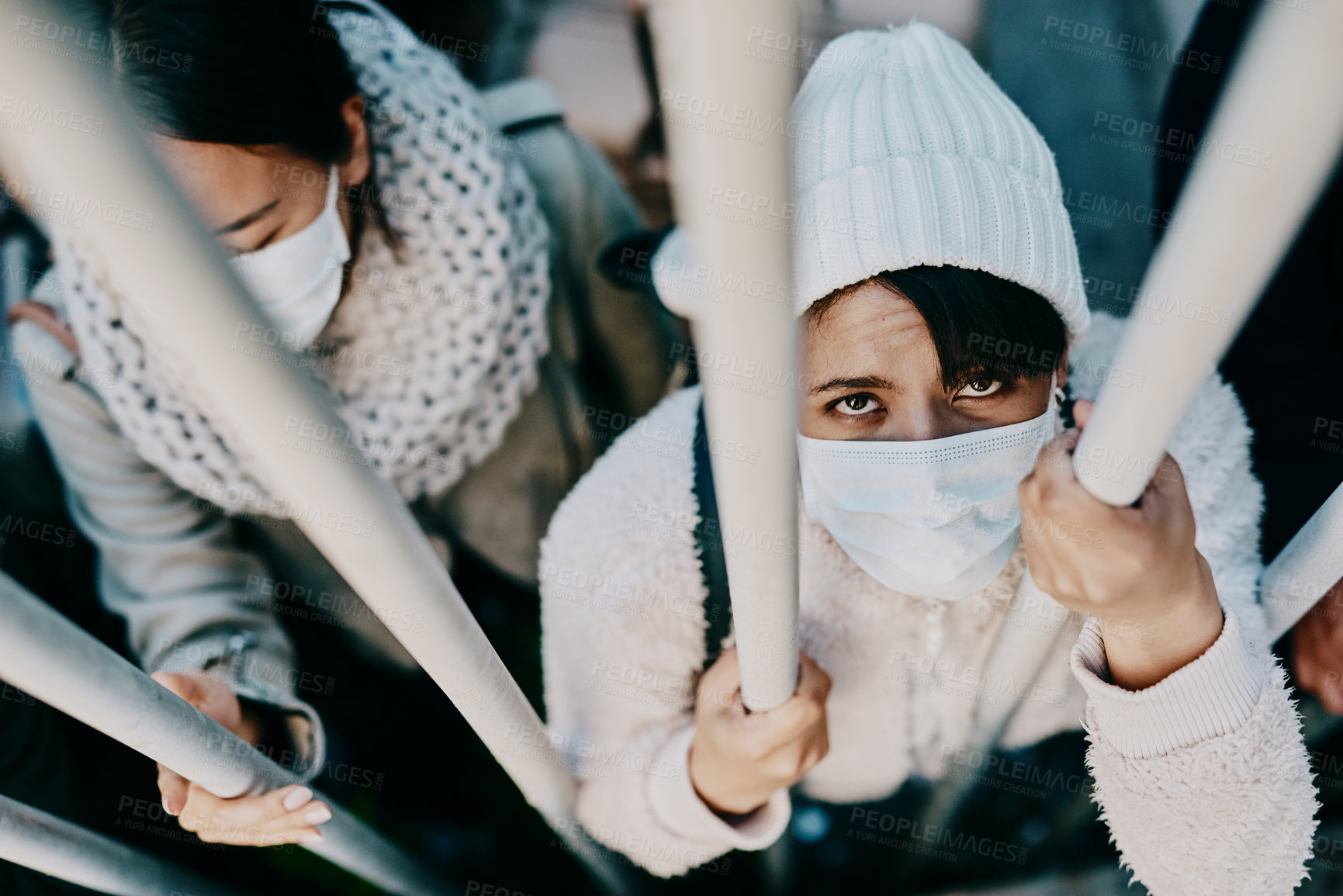 Buy stock photo Shot of a group of young people wearing masks while stuck behind a gate in a foreign city