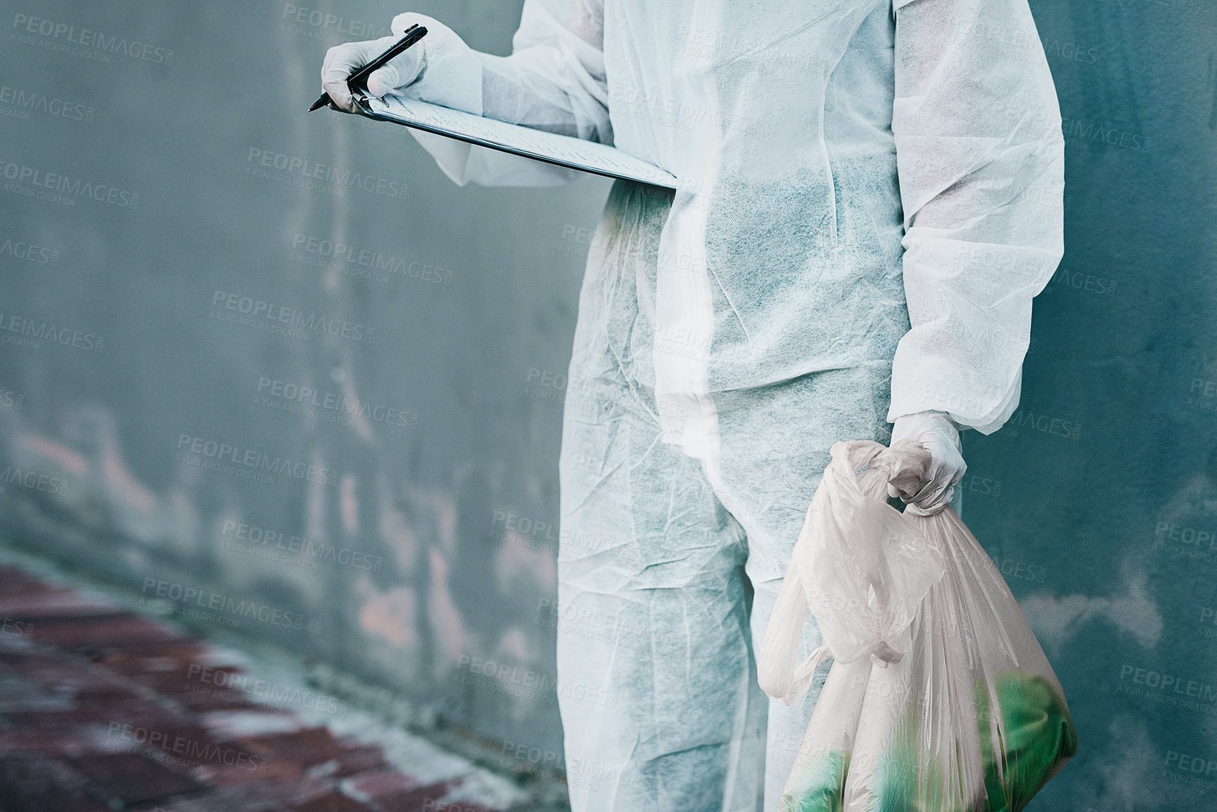 Buy stock photo Forensic investigator collecting evidence on a murder scene on a street holding a plastic bag and wearing a hazmat suit. Crime researcher doing a scientific criminal investigation outdoors in a city