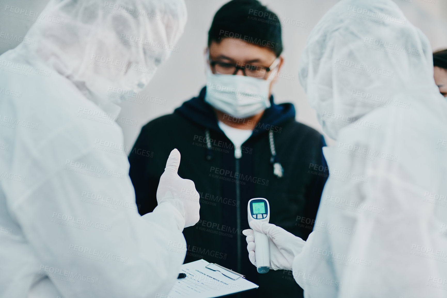 Buy stock photo Negative covid test and thumbs up for young man from healthcare worker after testing for virus. Medical professionals in hazmat suits taking temperature tests during disease outbreak or pandemic