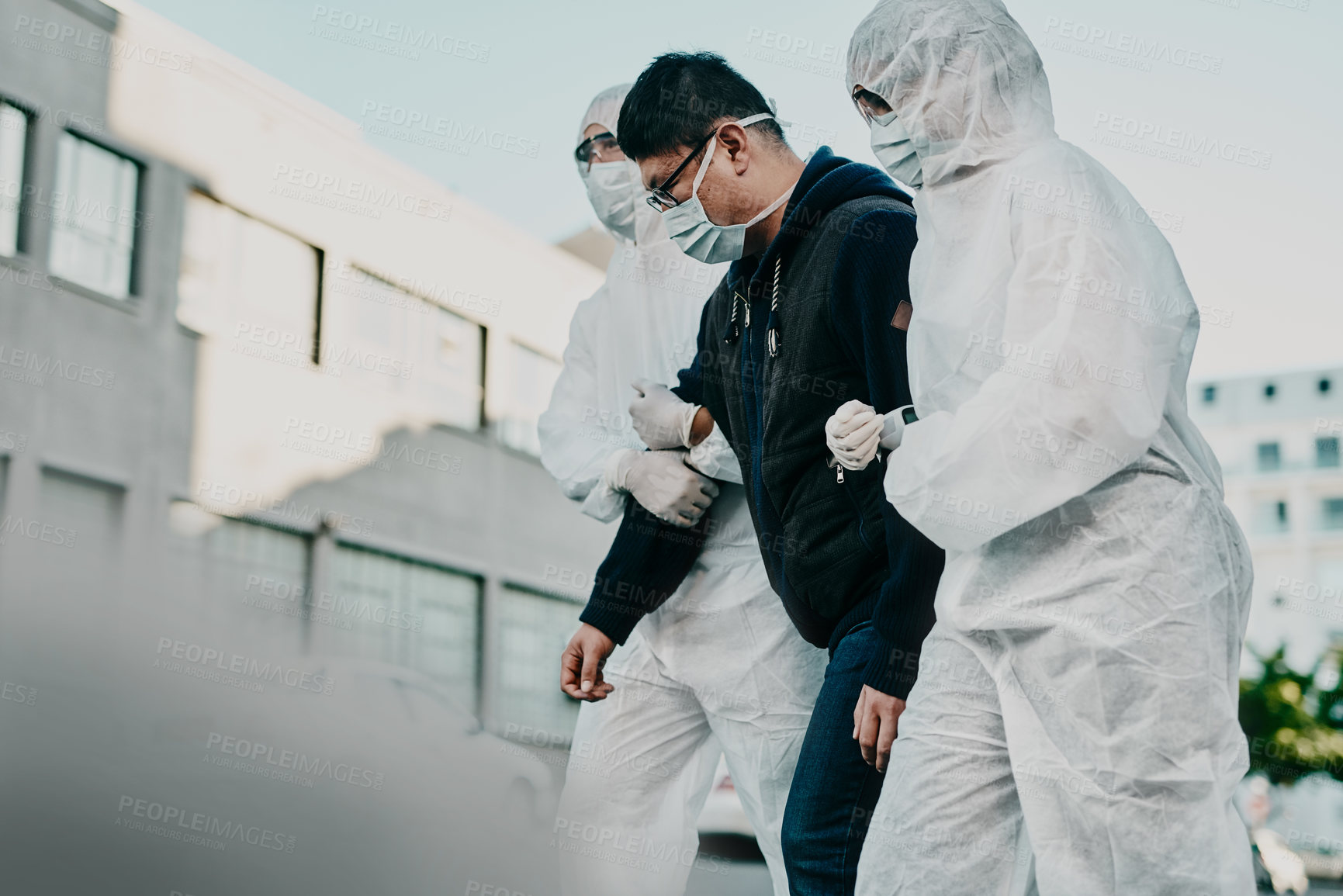 Buy stock photo Shot of a young man getting taken away by healthcare workers in hazmat suits during an outbreak