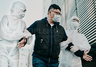 Buy stock photo Man breaking covid regulation getting taken away or arrested by healthcare workers wearing hazmat protective suits. Male removed for not following the rules or restrictions of coronavirus pandemic.
