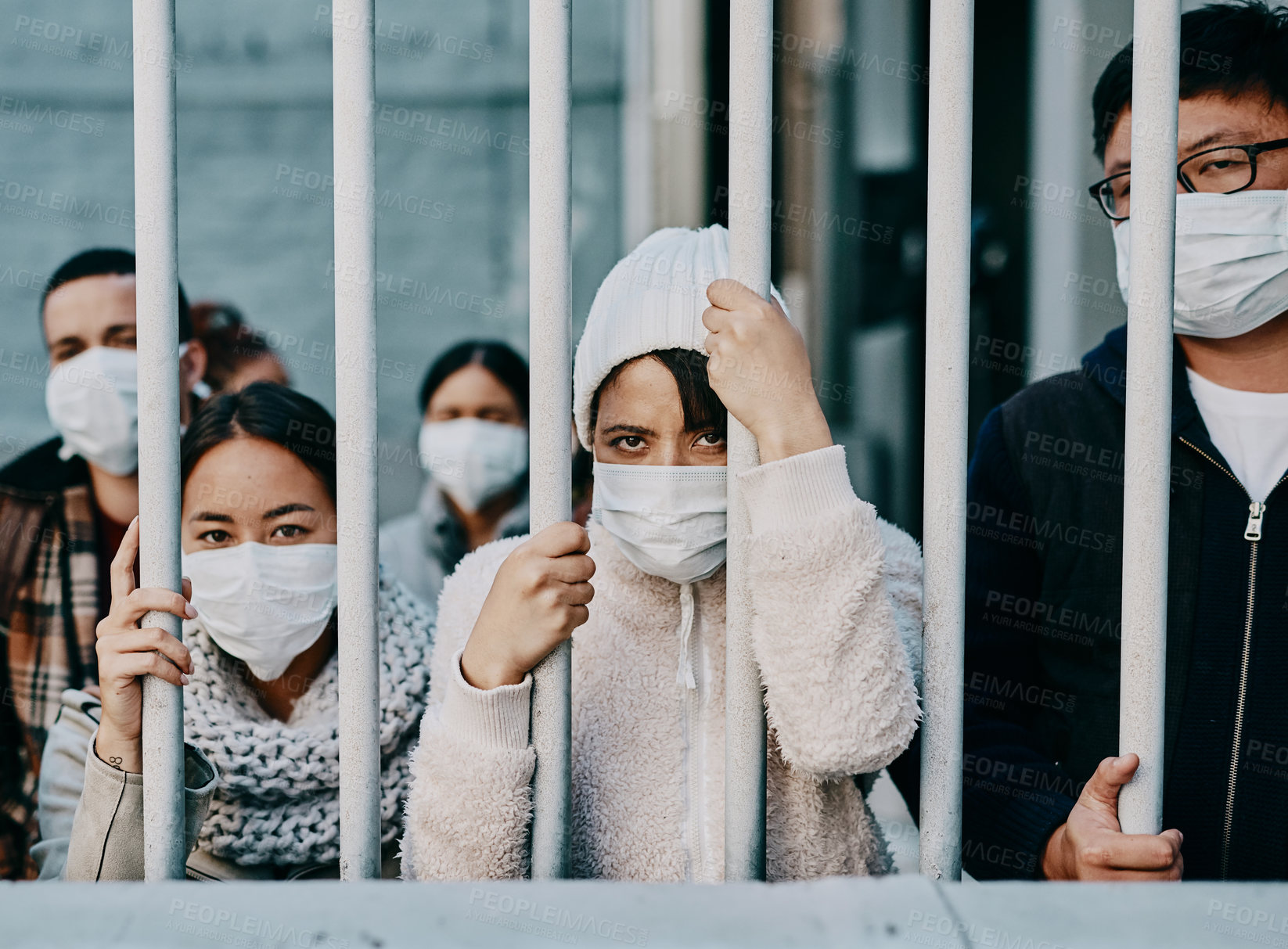 Buy stock photo Foreign people in isolation wearing covid face mask at the border or in quarantine or airport looking unhappy, upset and angry. Poor refugees, immigrants and tourists stuck behind a gate in lockdown