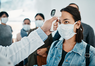 Buy stock photo Covid screening with a female tourist in a mask having her temperature taken with an infrared thermometer while waiting to board in an airport. Travel restrictions during the corona virus pandemic