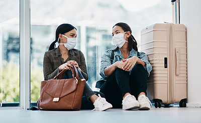 Buy stock photo Shot of two young women wearing masks while waiting together in an airport