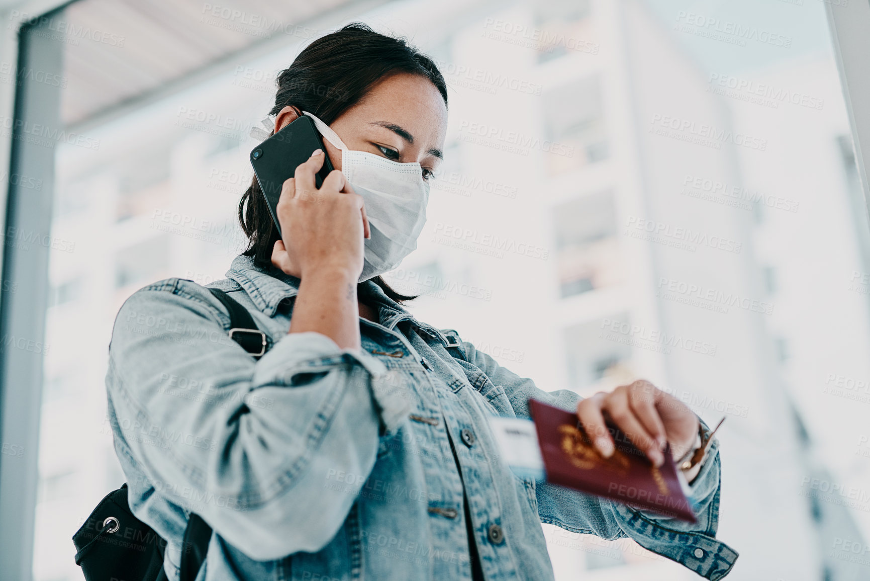 Buy stock photo Shot of a young woman wearing a mask, using a smartphone and checking the time in an airport