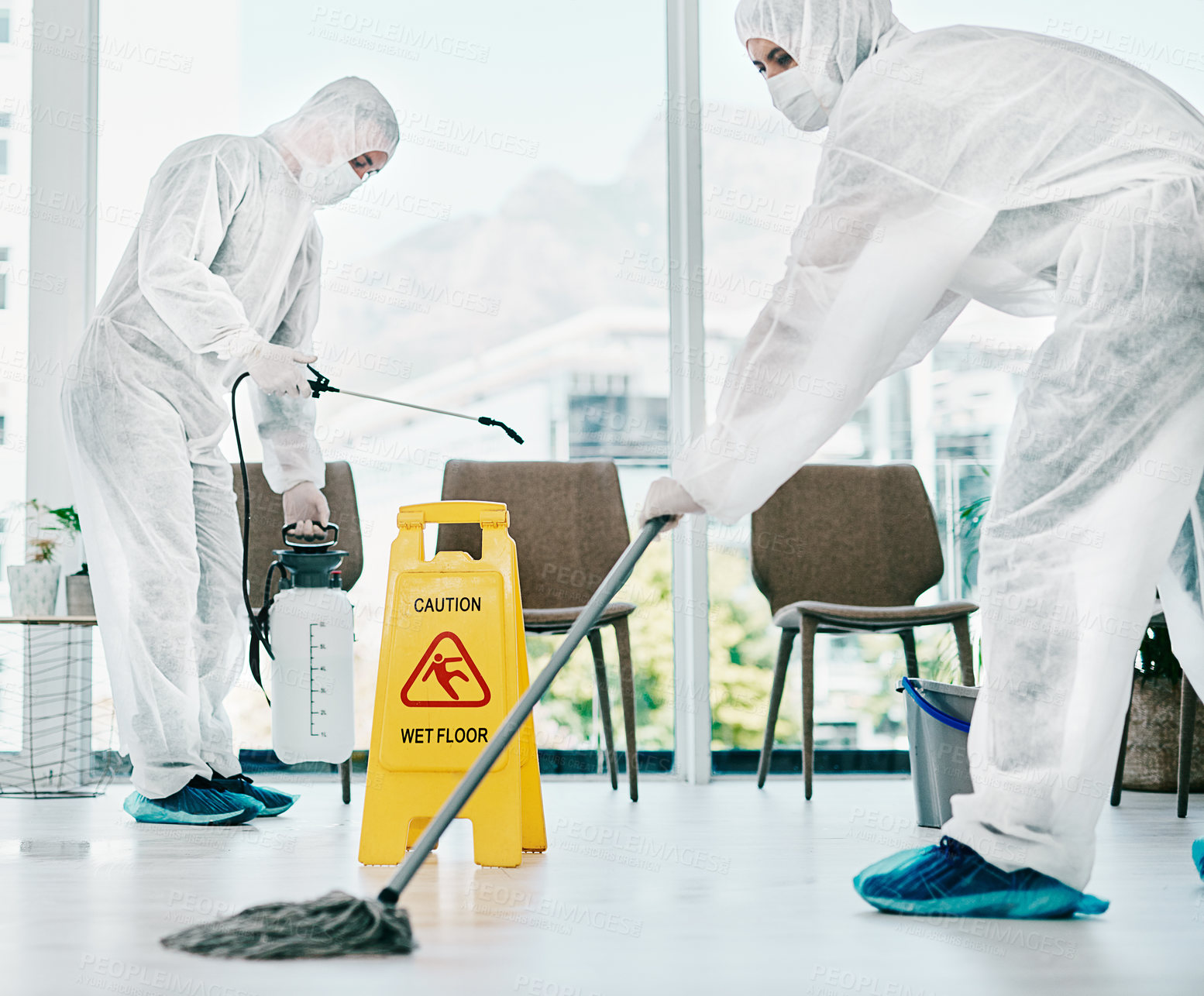 Buy stock photo Shot of healthcare workers wearing hazmat suits and sanitising a room during an outbreak