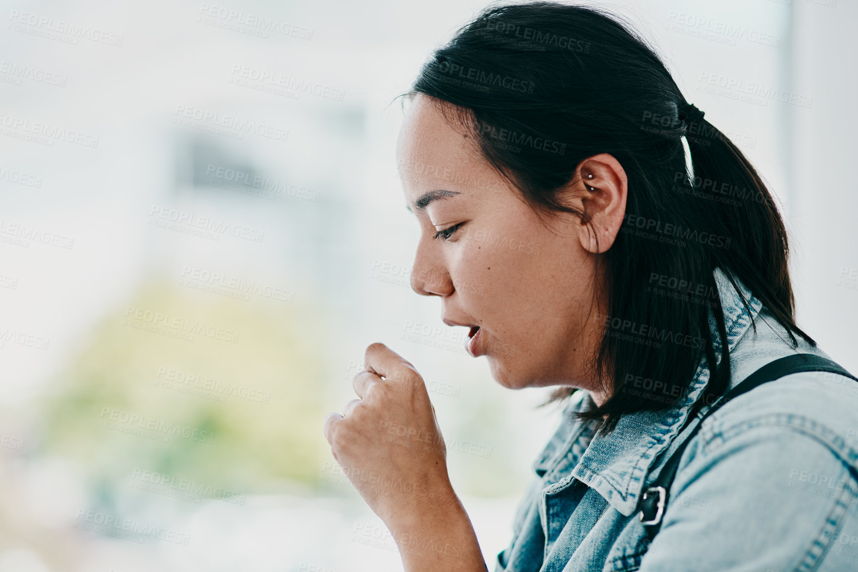 Buy stock photo Shot of a young woman coughing while waiting in a doctor’s office