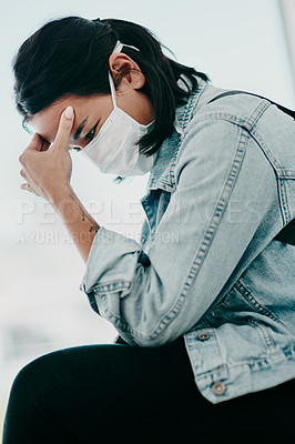 Buy stock photo Shot of a young woman experiencing a headache and wearing a mask while waiting in a doctor’s office
