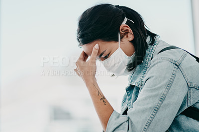 Buy stock photo Shot of a young woman experiencing a headache and wearing a mask while waiting in a doctor’s office
