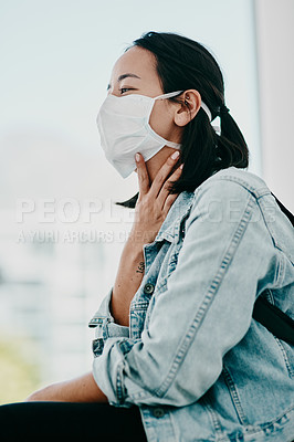 Buy stock photo Shot of a young woman wearing a mask and suffering from throat pain in a doctor’s office